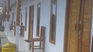 A corridor with wooden doors and benches, a tiled floor, and a yellow fire extinguisher. - Menjangan Hostel (Pejarakan)