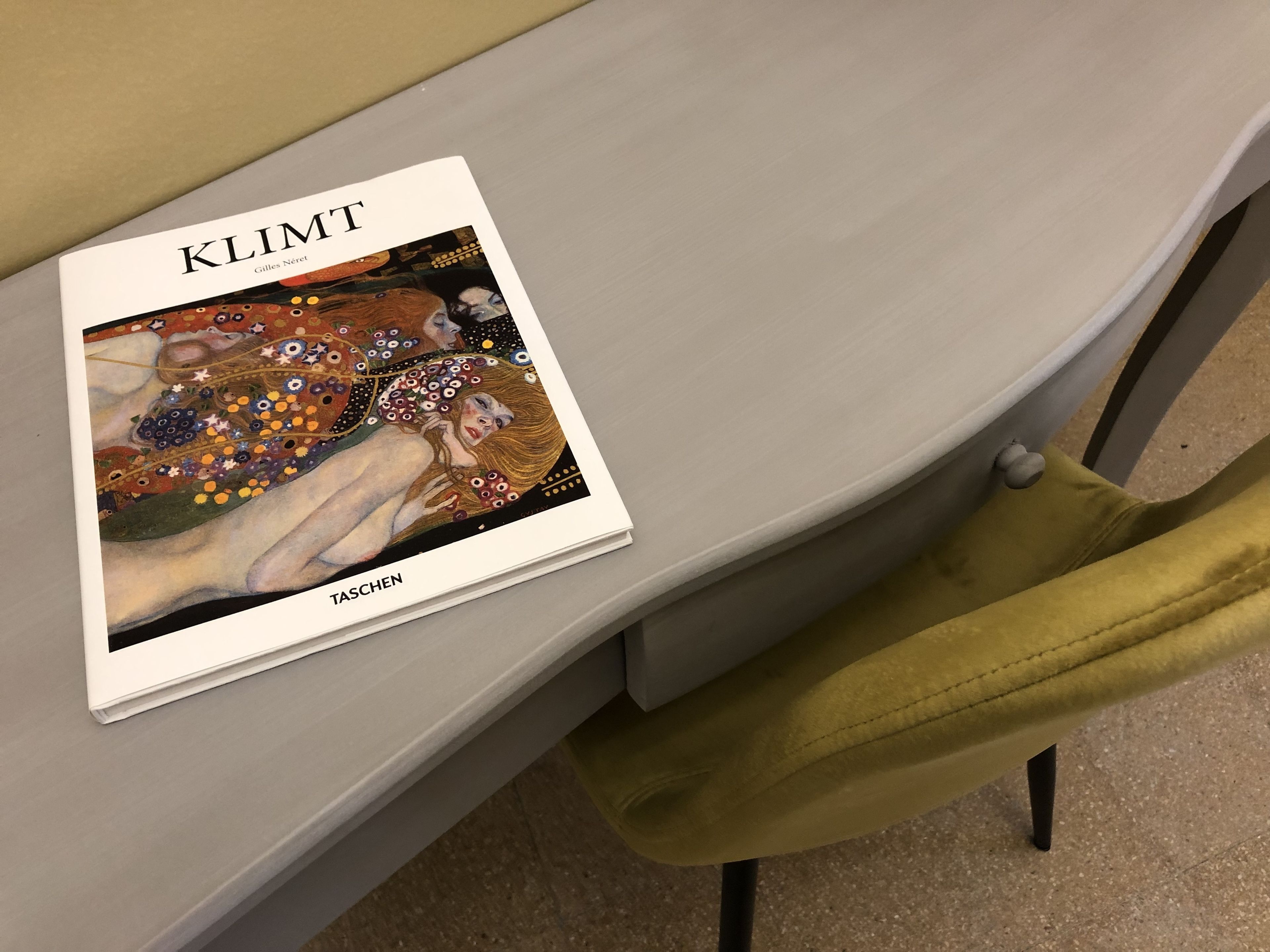 A book titled 'KLIMT' with a colorful illustration on its cover, placed on a white table.