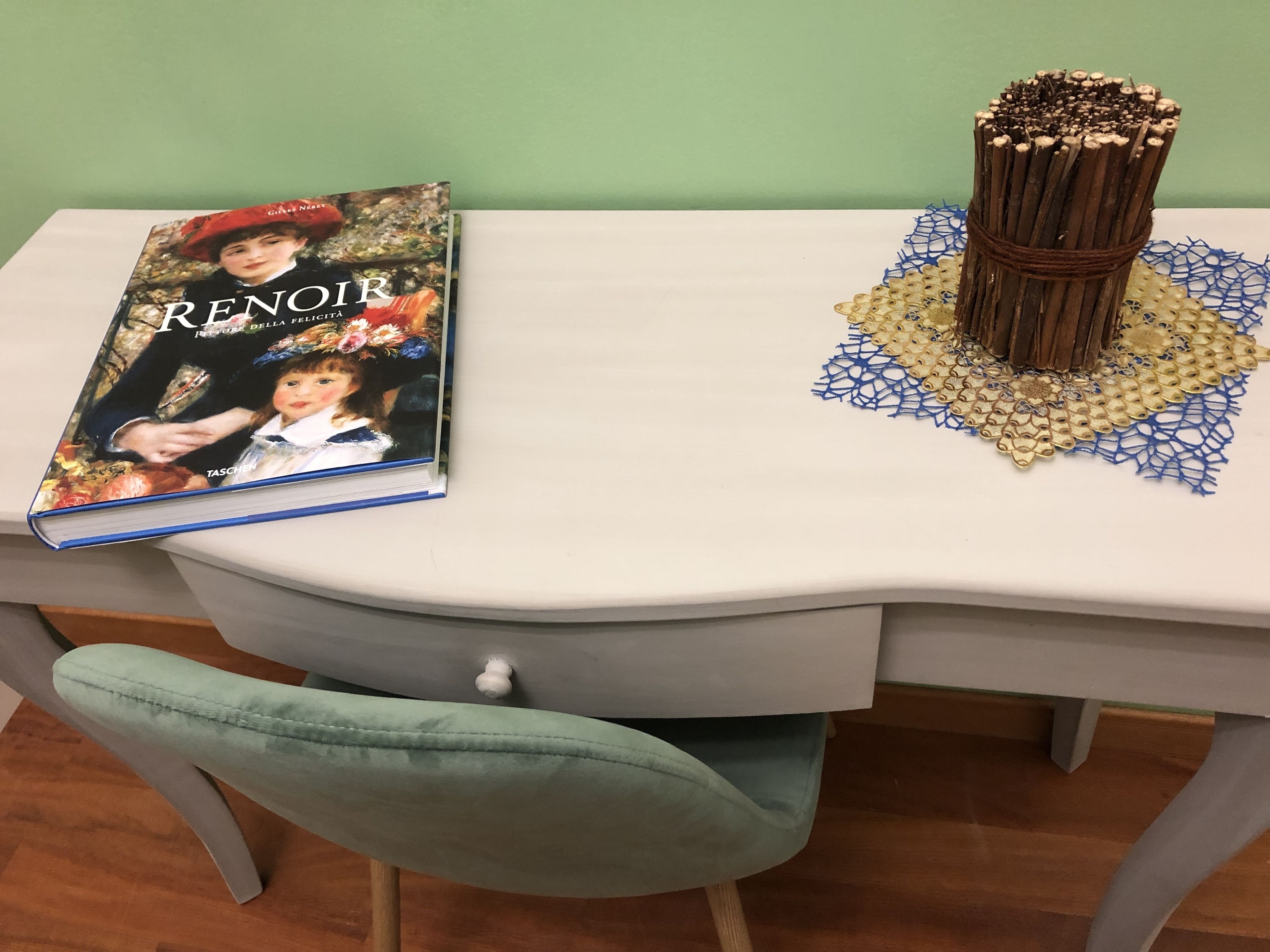 A white table with a book titled 'Renoir' and a decorative object on it.