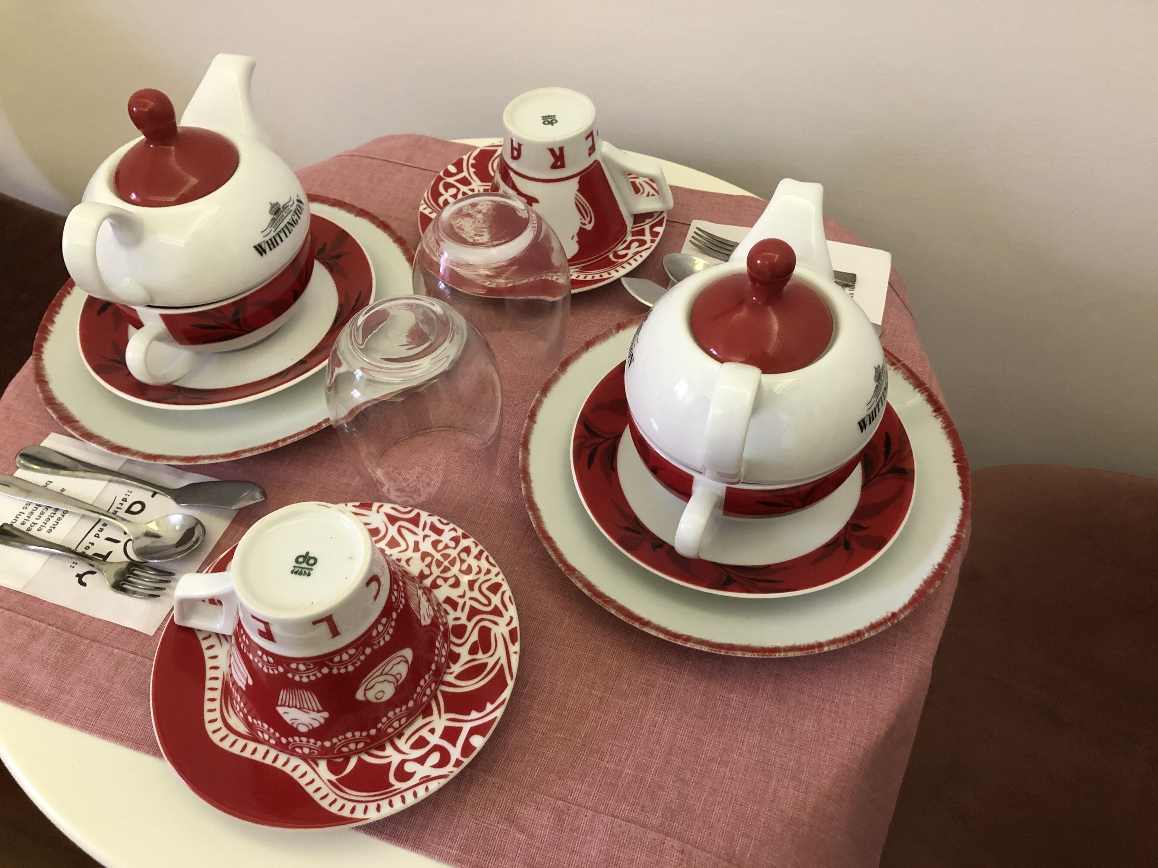 Una mesa dispuesta con servicio de té, incluyendo teteras, tazas, platillos y azucarero, todo con un diseño rojo y blanco.