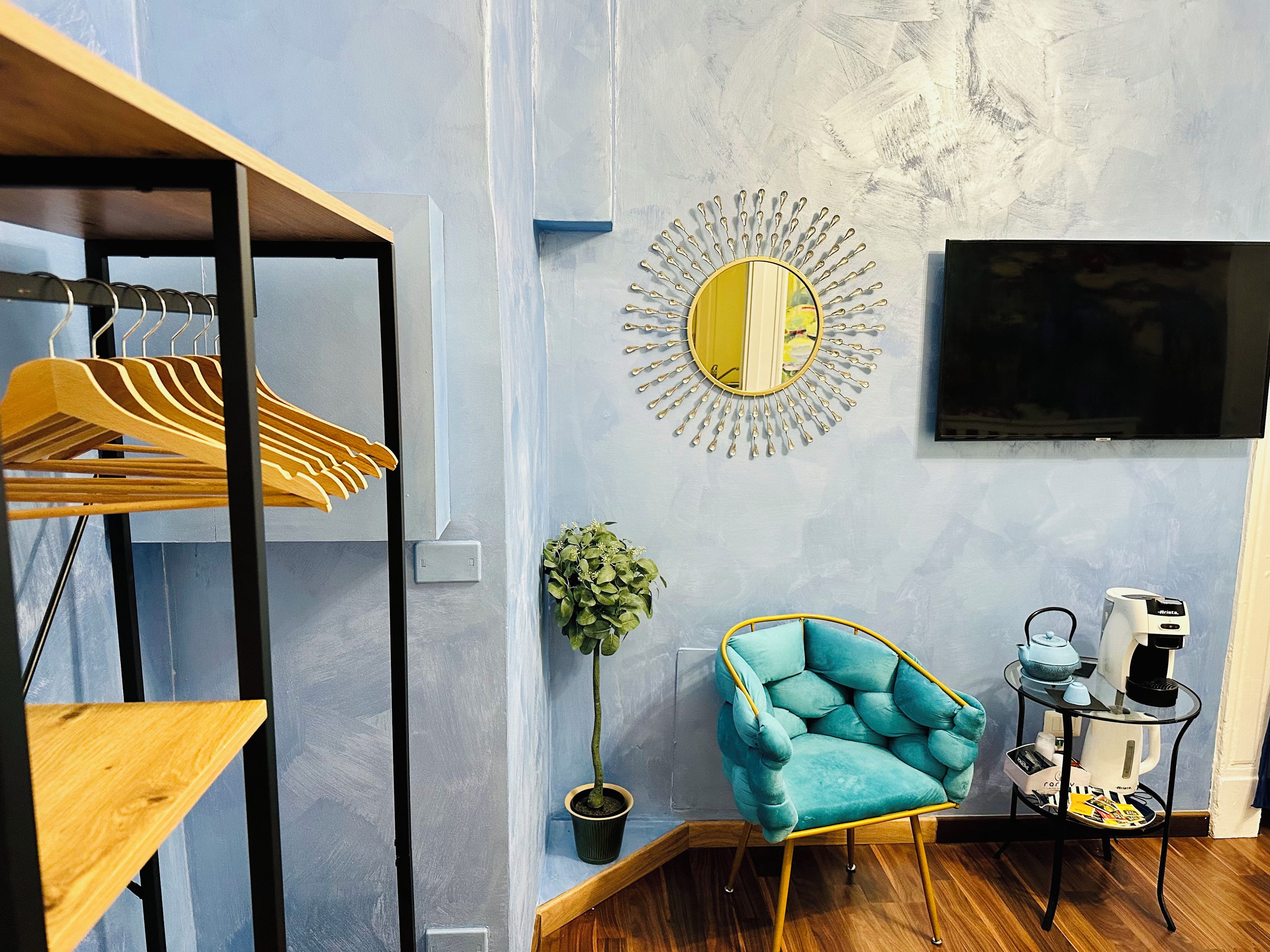 Un soggiorno moderno con una poltrona blu, uno specchio rotondo, un televisore e una macchina da caffè.