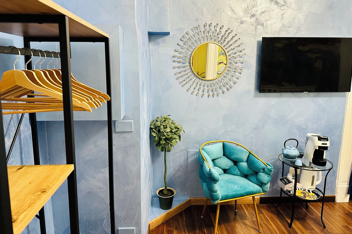 Ein modernes Wohnzimmer mit einem blauen Sessel, einem runden Spiegel, einem Fernseher und einer Kaffeemaschine.
