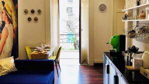 A room with a dining area, a kitchen with a coffee machine, and a view through an open door.