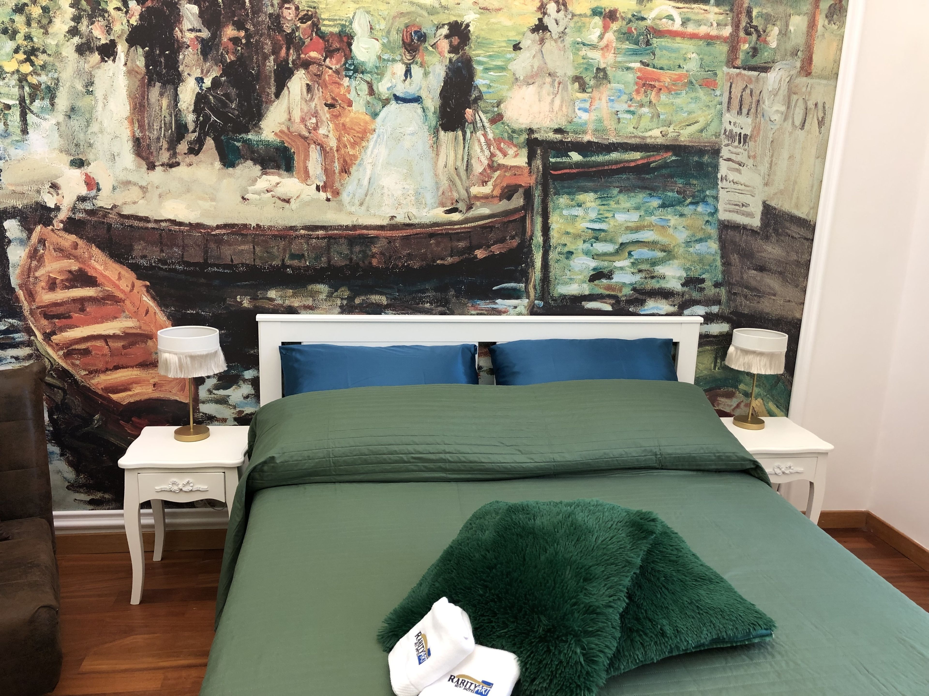 Un dormitorio con un cuadro grande en la pared, una cama con ropa de cama verde, dos mesitas de noche con lámparas, y un edredón verde mullido sobre la cama.