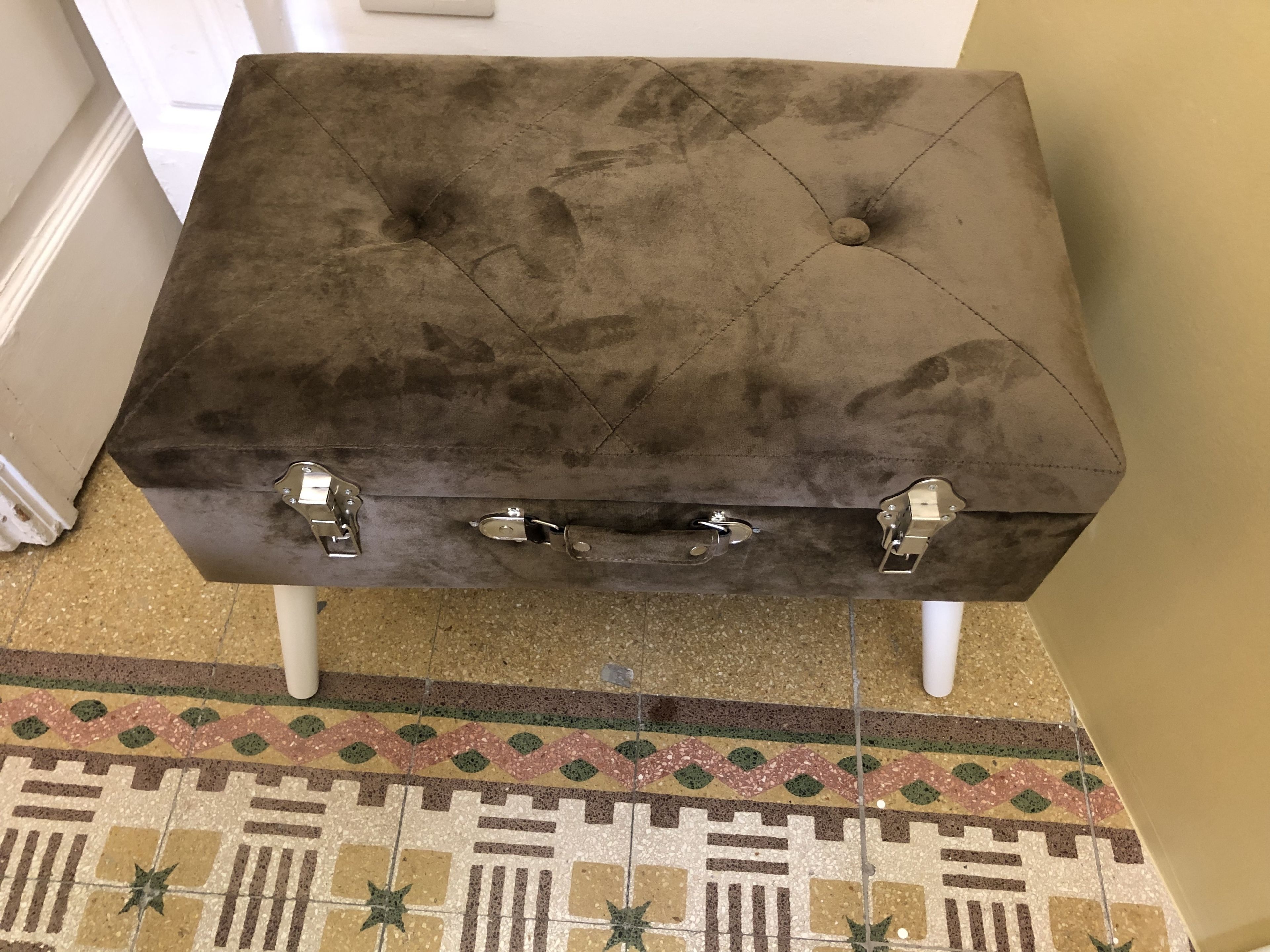 A brown upholstered ottoman with metal hardware, positioned on a patterned rug.