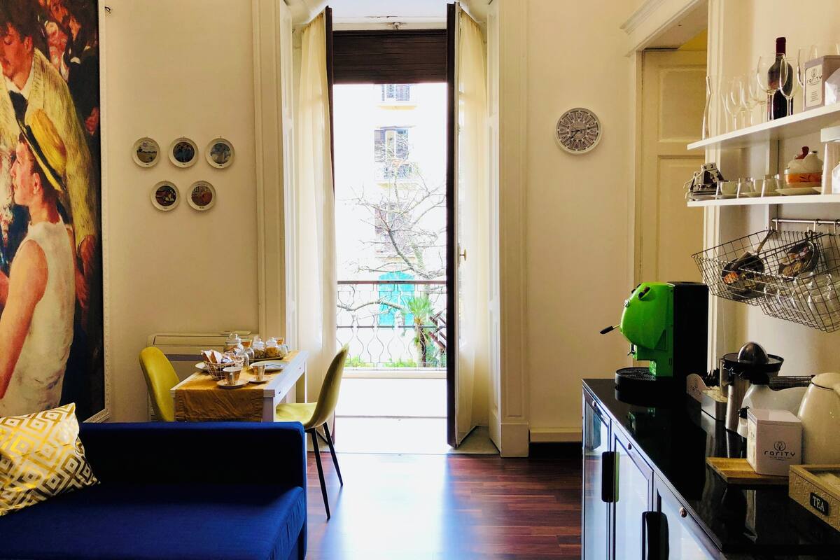 A room with a dining area, a kitchen, and a large painting on the wall.