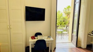 A room with a desk, a chair, a television, and a view of a balcony with outdoor furniture.