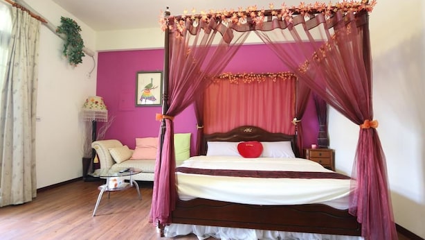 A four-poster bed with a canopy, a small bedside table, a chair, and a wall-mounted shelf with a plant. - Shuishang Ya Ju Homestay (Hualien City)