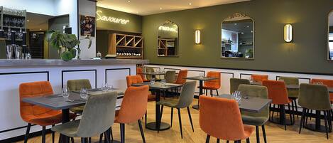 Restaurante com várias mesas e cadeiras, um espaço de bar e um espelho grande na parede.