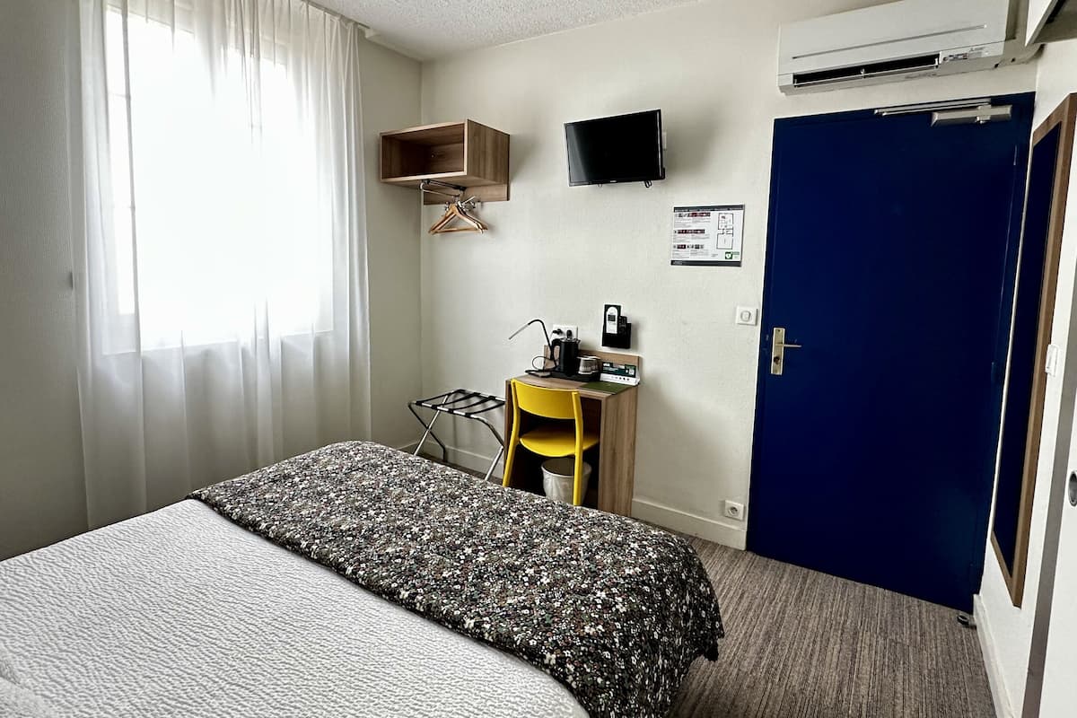 Habitación de hotel con cama, escritorio con silla, televisor y aire acondicionado.