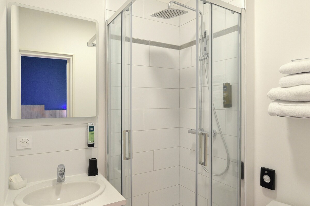 A modern bathroom with a glass-enclosed shower, a white sink, and a mirror.