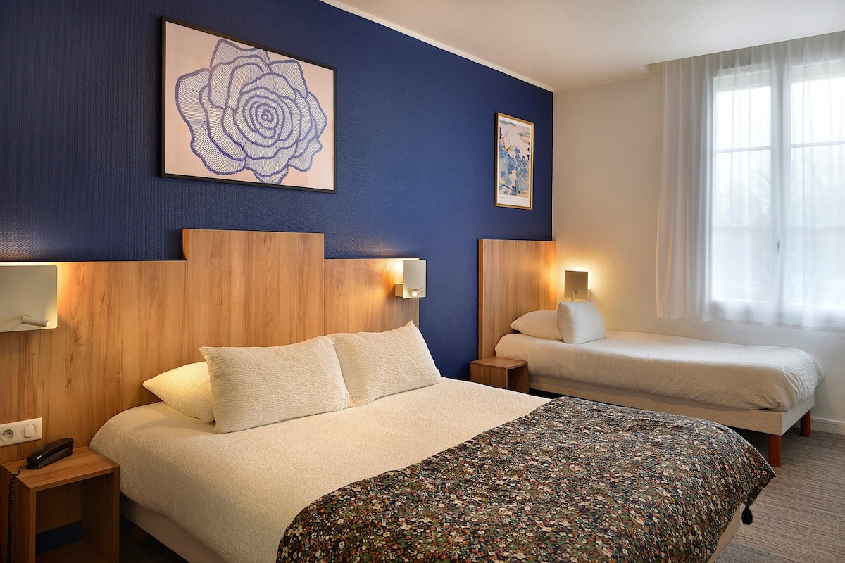 Una habitación de hotel con una cama grande, una cama más pequeña, cabeceros de madera y obras de arte en las paredes.