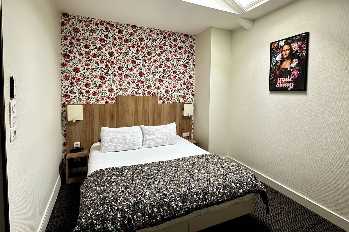 Una habitación de hotel con cabecera de flores, cama con colcha floral, tragaluz y un cartel en la pared.
