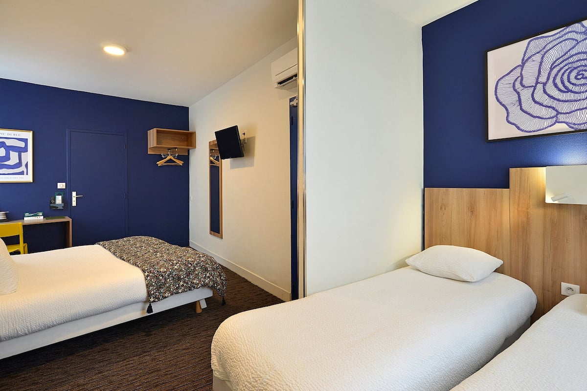 Habitación de hotel con dos camas, cabecera de madera, televisor montado en la pared y puerta con barra para toallas.