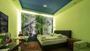 A bedroom with a bed, a desk, a chair, and a window with a forest mural.