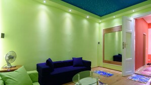 A room with a green wall, a blue sofa, a glass table, and a mirror.