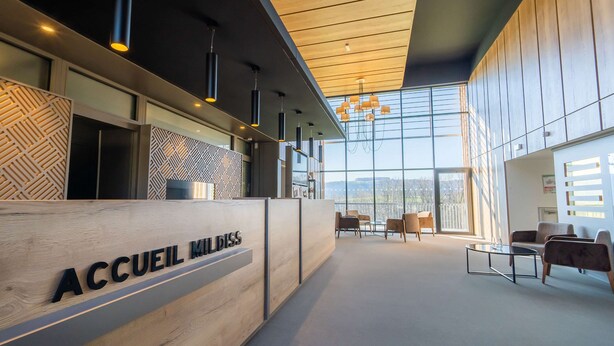 A reception area with a wooden reception desk labeled "ACCUEIL MILDISS," modern pendant lighting, and a seating area with chairs and a table. - Mildiss Hotel Spa & Restaurant, BW Signature Collection (Besse-et-Saint-Anastaise)