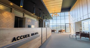 A reception area with a wooden reception desk labeled "ACCUEIL MILDISS," modern pendant lighting, and a seating area with chairs and a table.