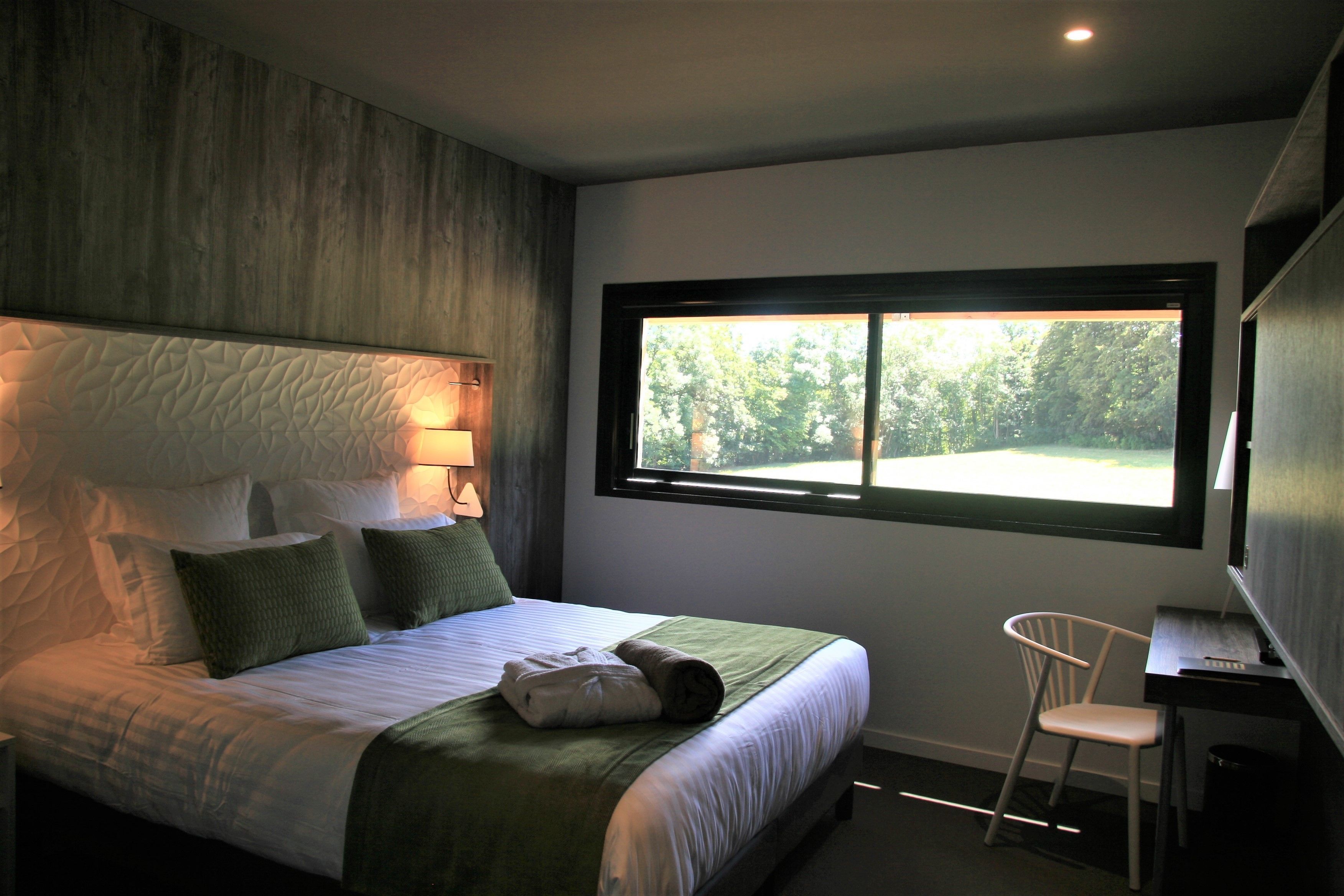 Un dormitorio moderno con una cama grande, un escritorio y una ventana con vistas a árboles.