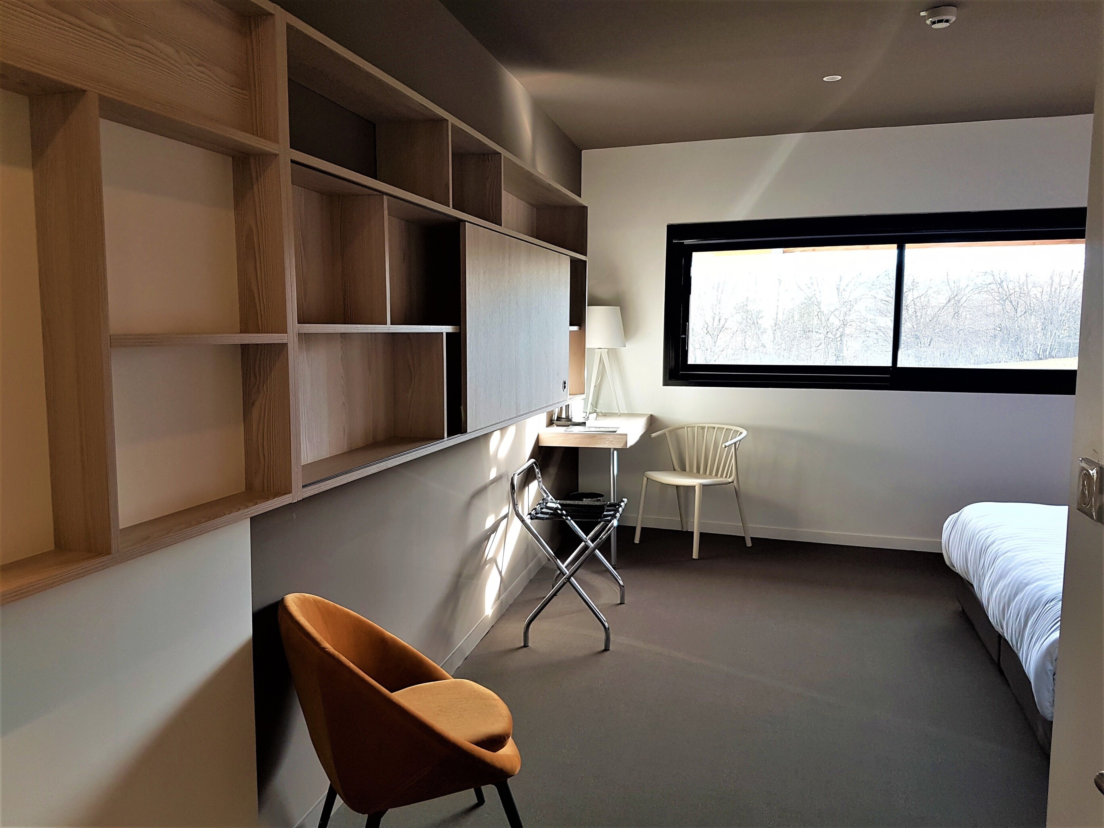 A modern bedroom with a bed, a desk, a chair, and built-in shelving.