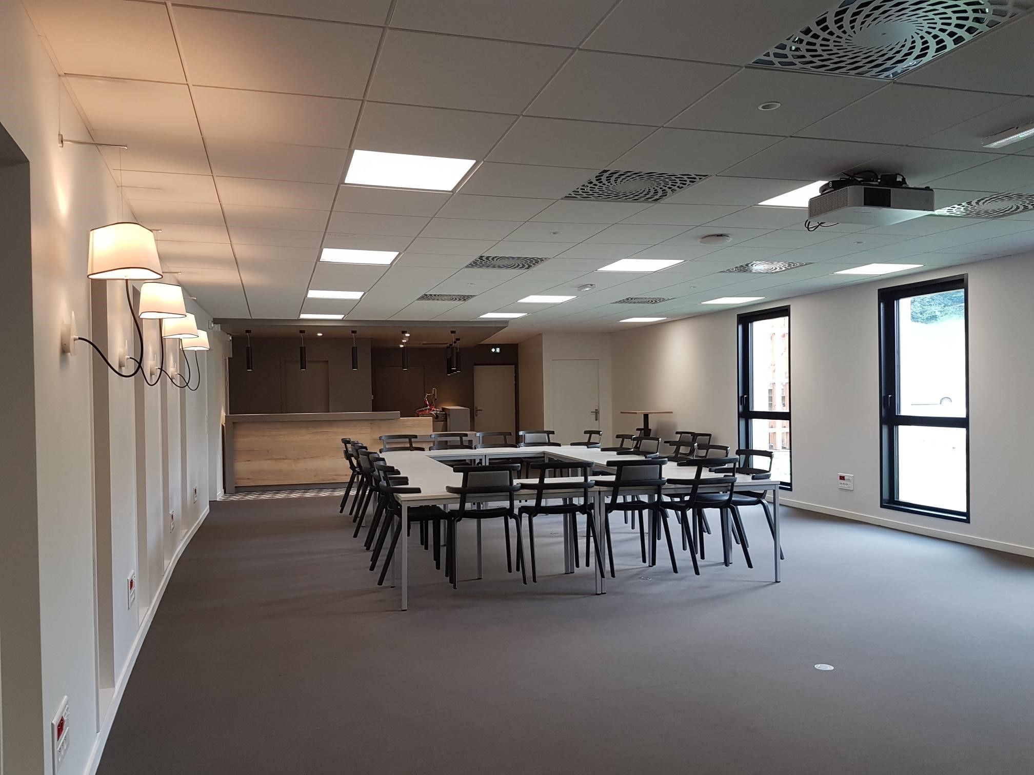 A conference room with a long table and chairs, ceiling lights, and large windows.
