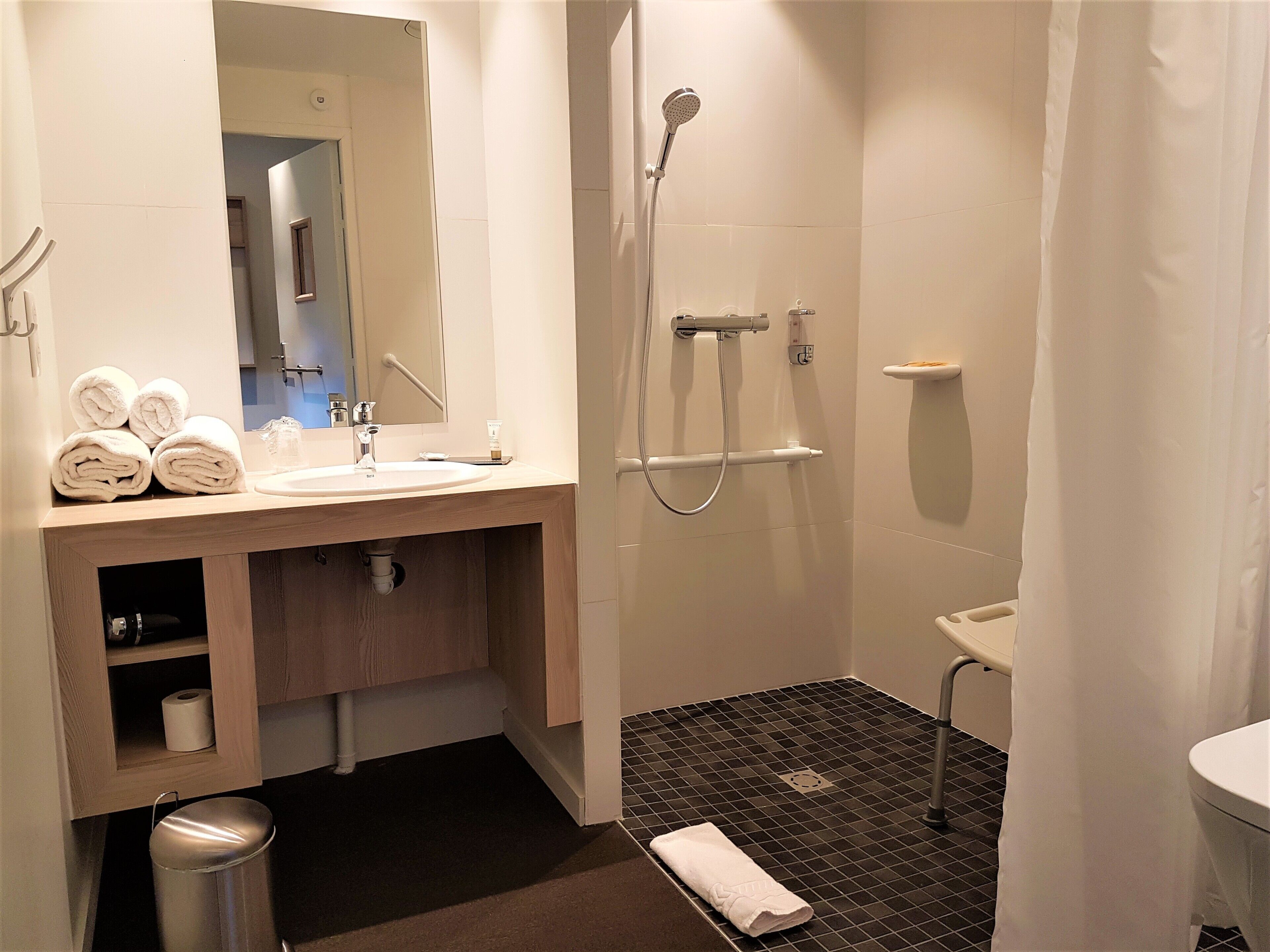 A modern bathroom with a sink, mirror, towel rack, shower, and toilet.