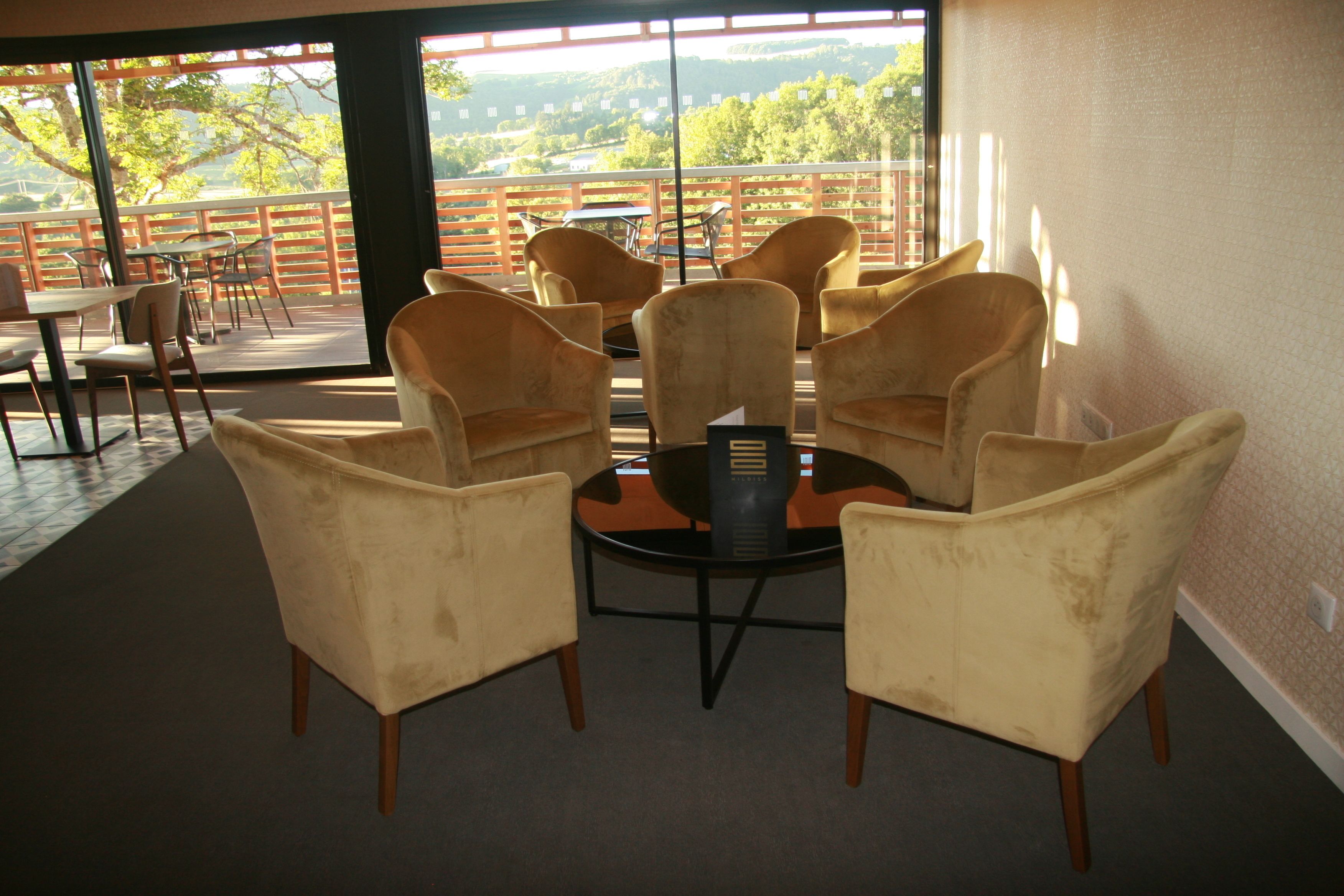 A seating area with four armchairs and a small round table, a wooden floor, and a view of a balcony with tables and chairs.