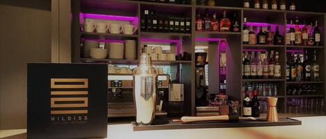 Zona de bar con estantes llenos de botellas de licores y una máquina de café.