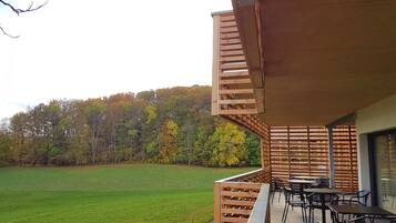 Una terraza de madera con mobiliario exterior y vistas a un campo cubierto de hierba y árboles.