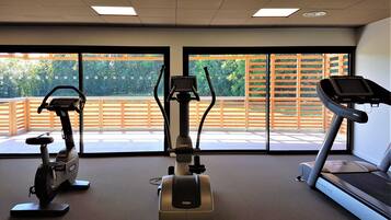 A gym with stationary bikes, a treadmill, and large windows with a view of greenery.