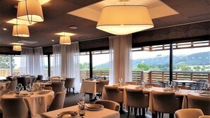 A restaurant with round tables, white tablecloths, and hanging pendant lights. - Mildiss Hotel Spa & Restaurant, BW Signature Collection (Besse-et-Saint-Anastaise)