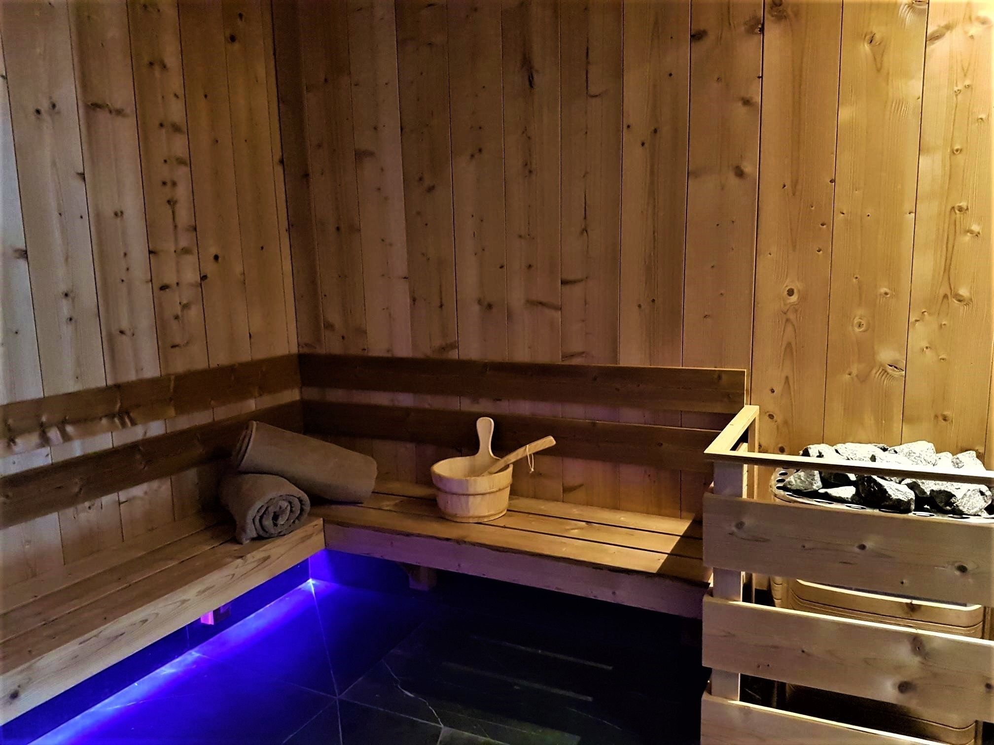 A wooden sauna with a bench, a wooden bucket, and a stone-filled container.