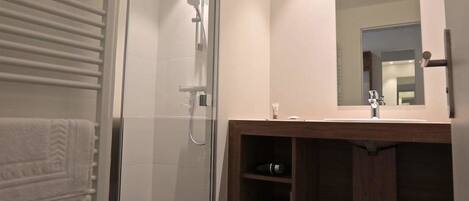 Un baño moderno con ducha de vidrio, tocador de madera con espejo y piso oscuro.