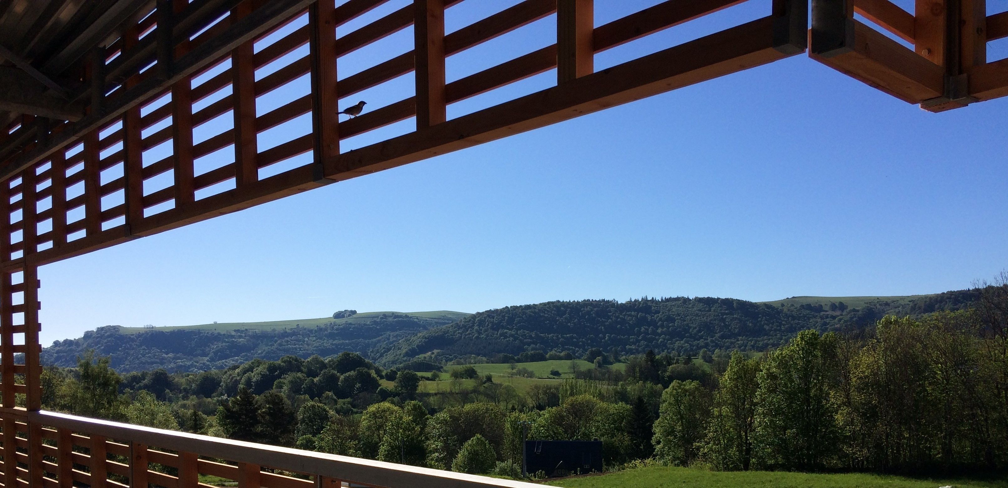 Eine hölzerne Pergola mit Blick auf ein üppiges Tal, sanfte Hügel und dichte Wälder.