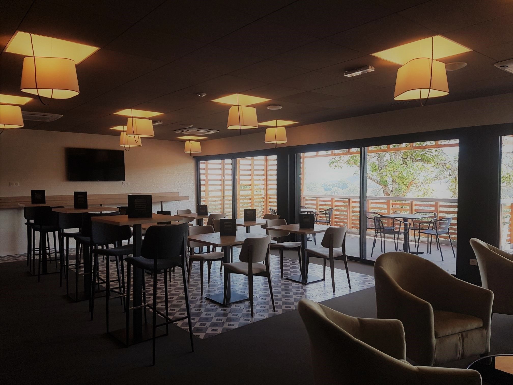 A modern dining area with tables and chairs, large windows, and pendant lighting.