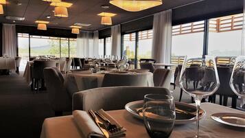 A restaurant with tables set for dining, large windows, and hanging pendant lights.
