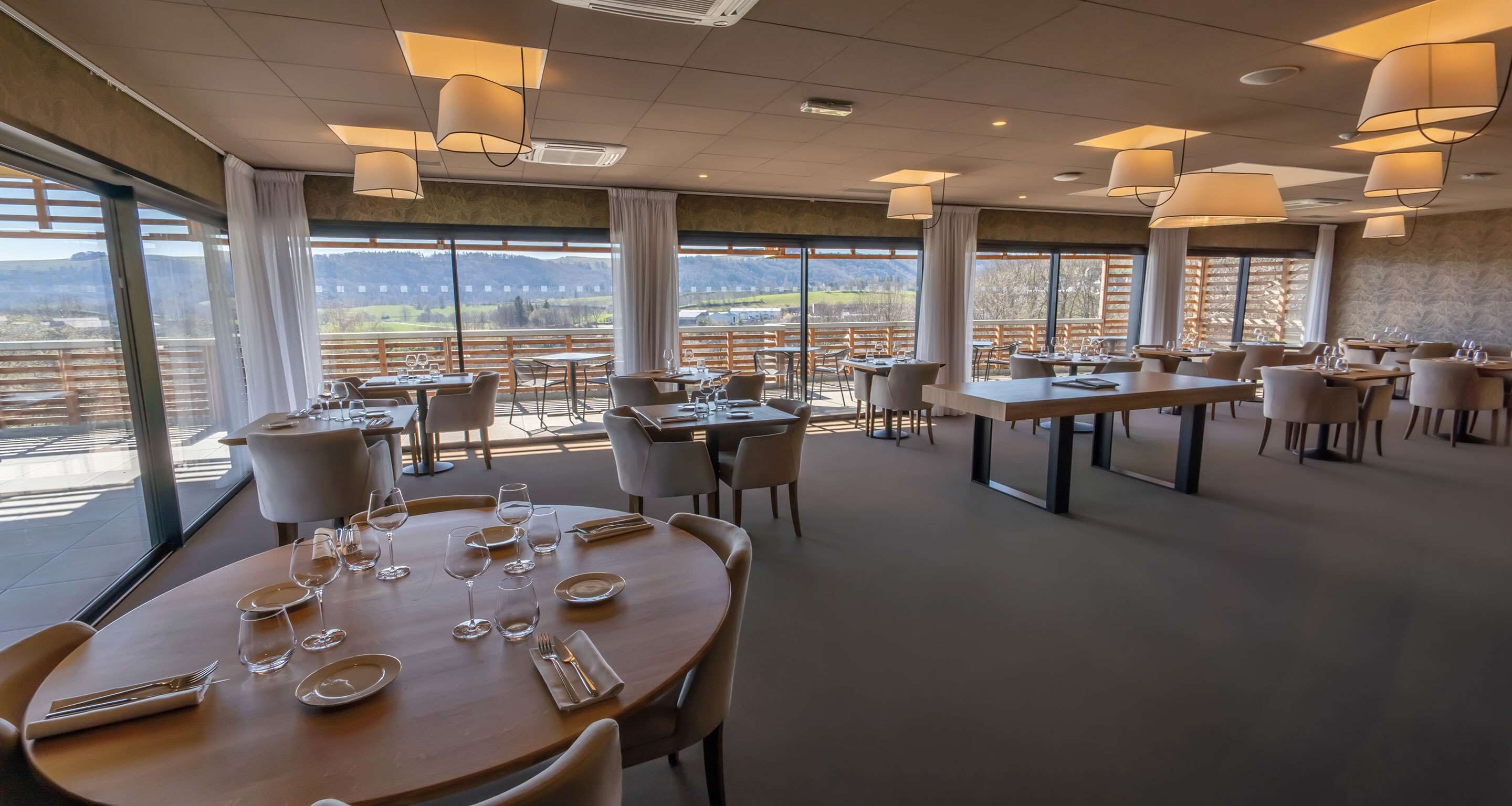 A restaurant with round tables, chairs, and hanging lamps.