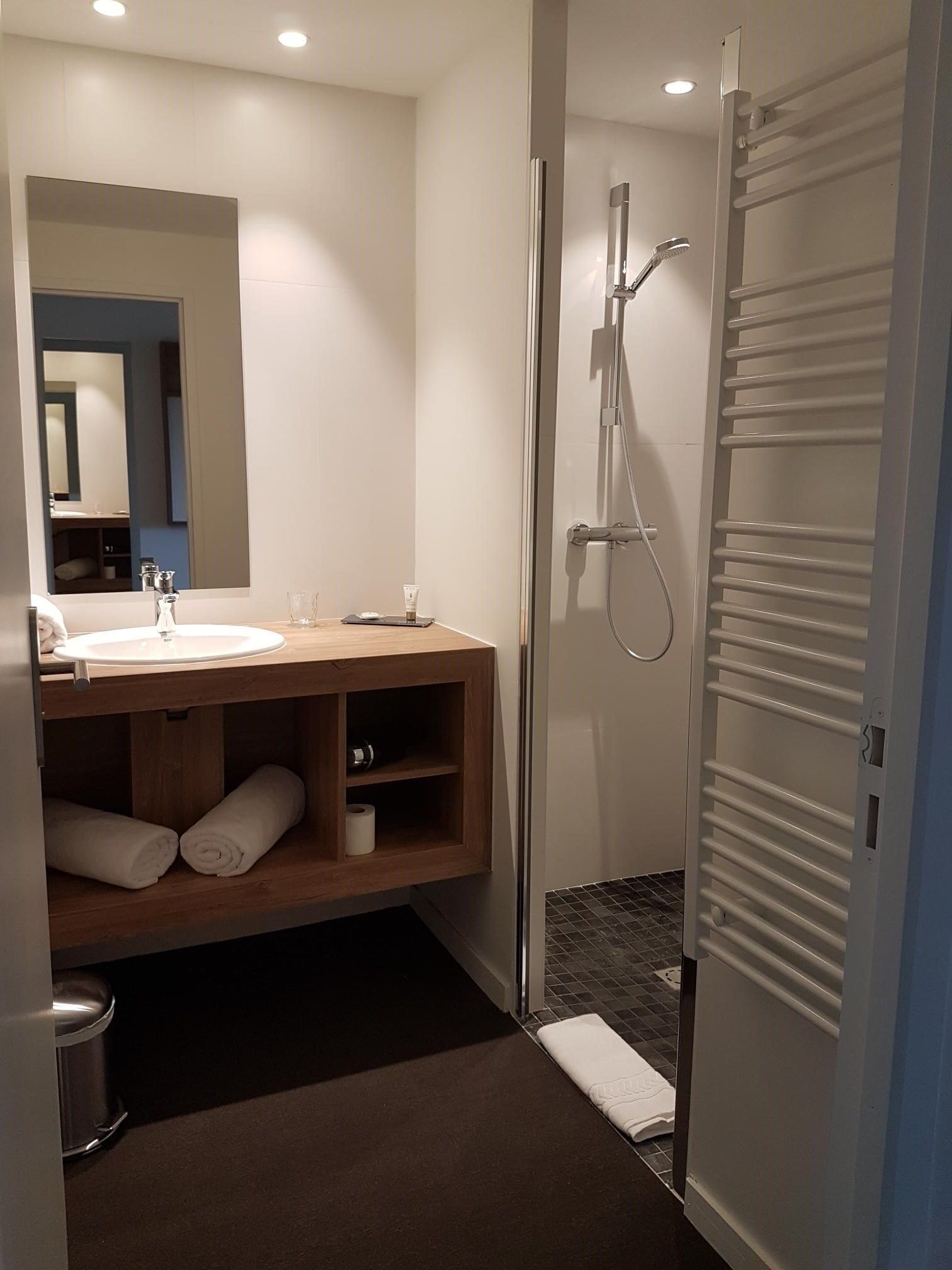 A modern bathroom with a wooden vanity, a large mirror, a shower, and a towel rack.