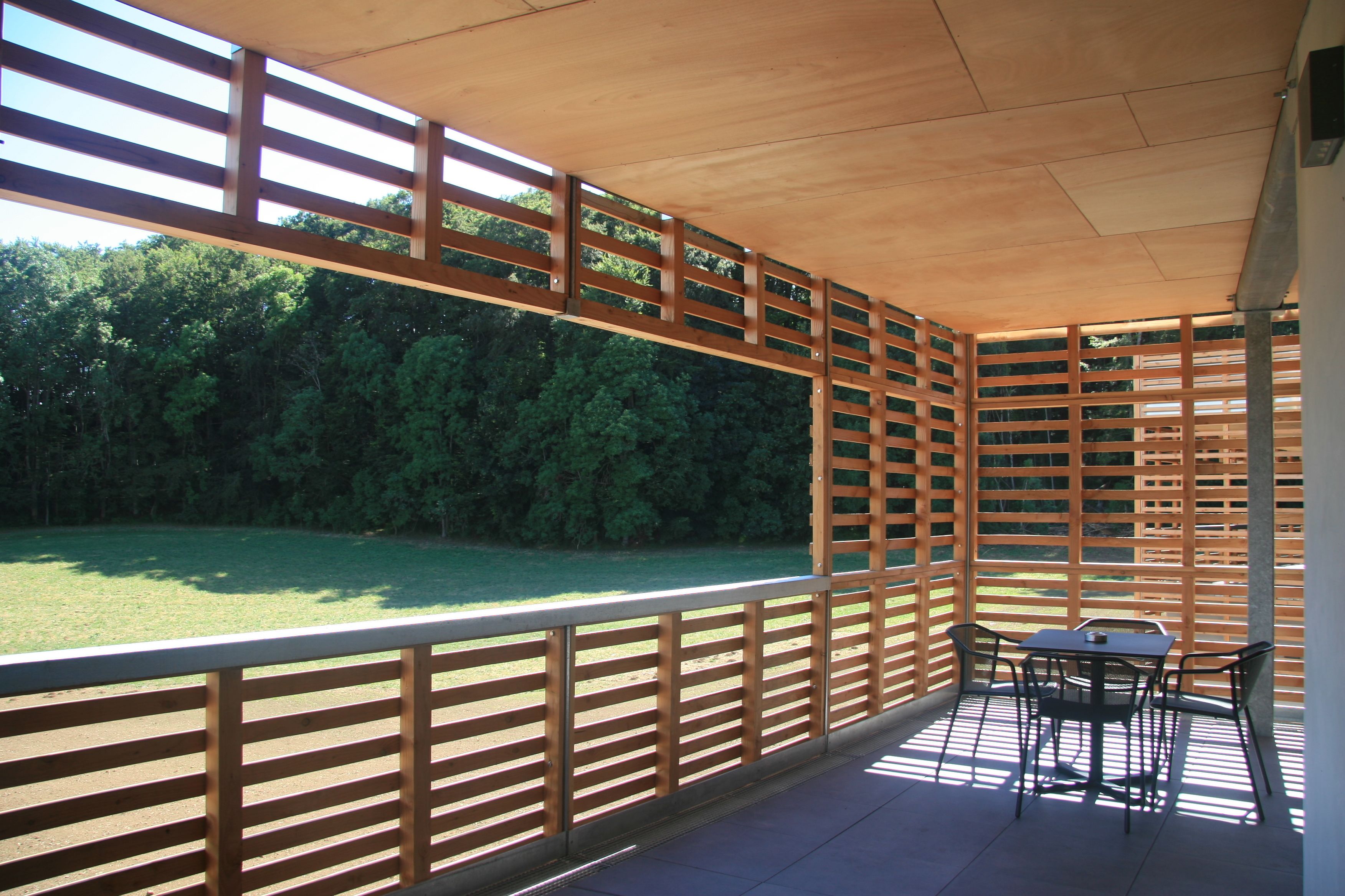 Un patio couvert avec une table et des chaises, une clôture en bois et une vue sur une zone herbeuse et des arbres.