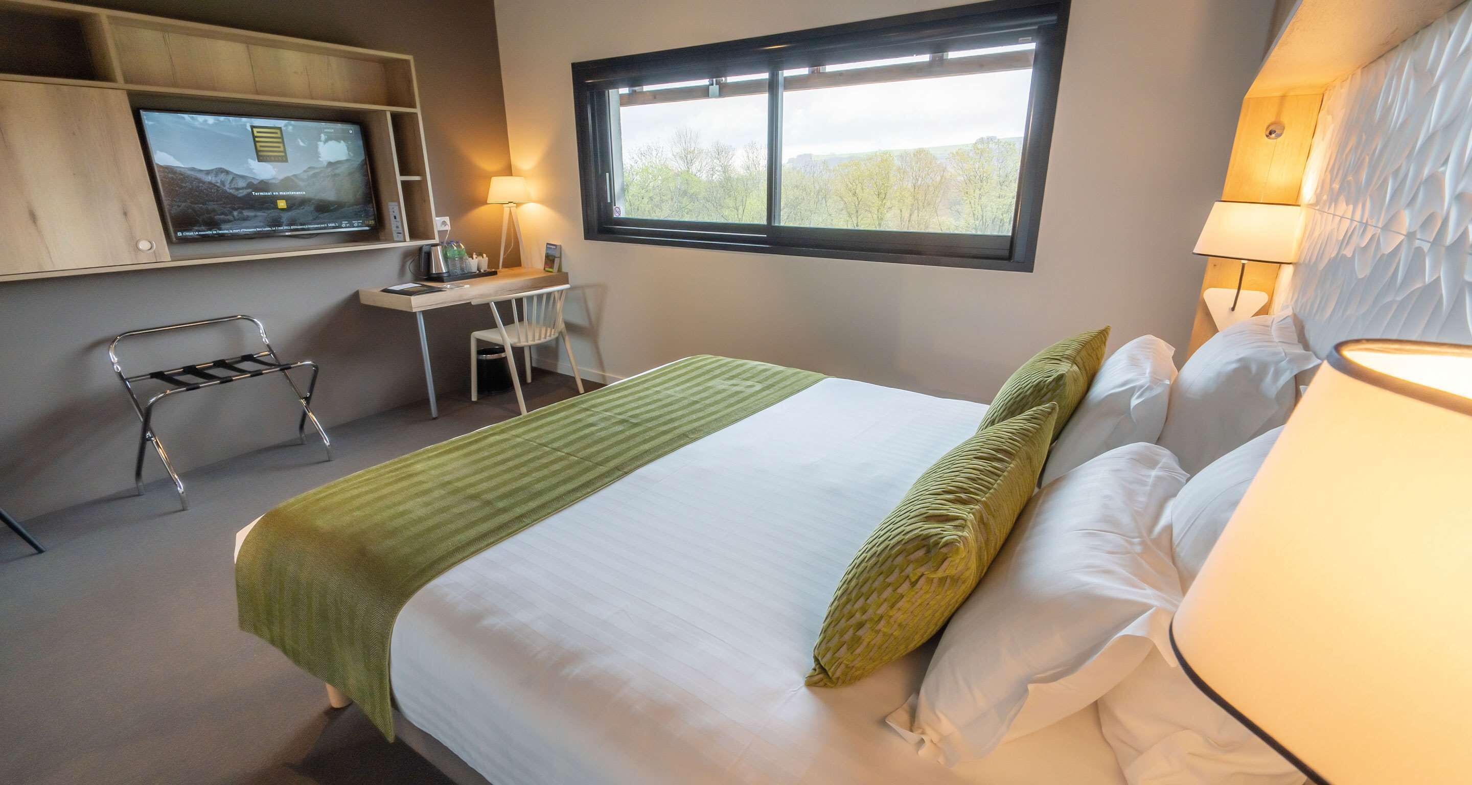 Una habitación de hotel con cama, escritorio, silla, televisión y ventana.