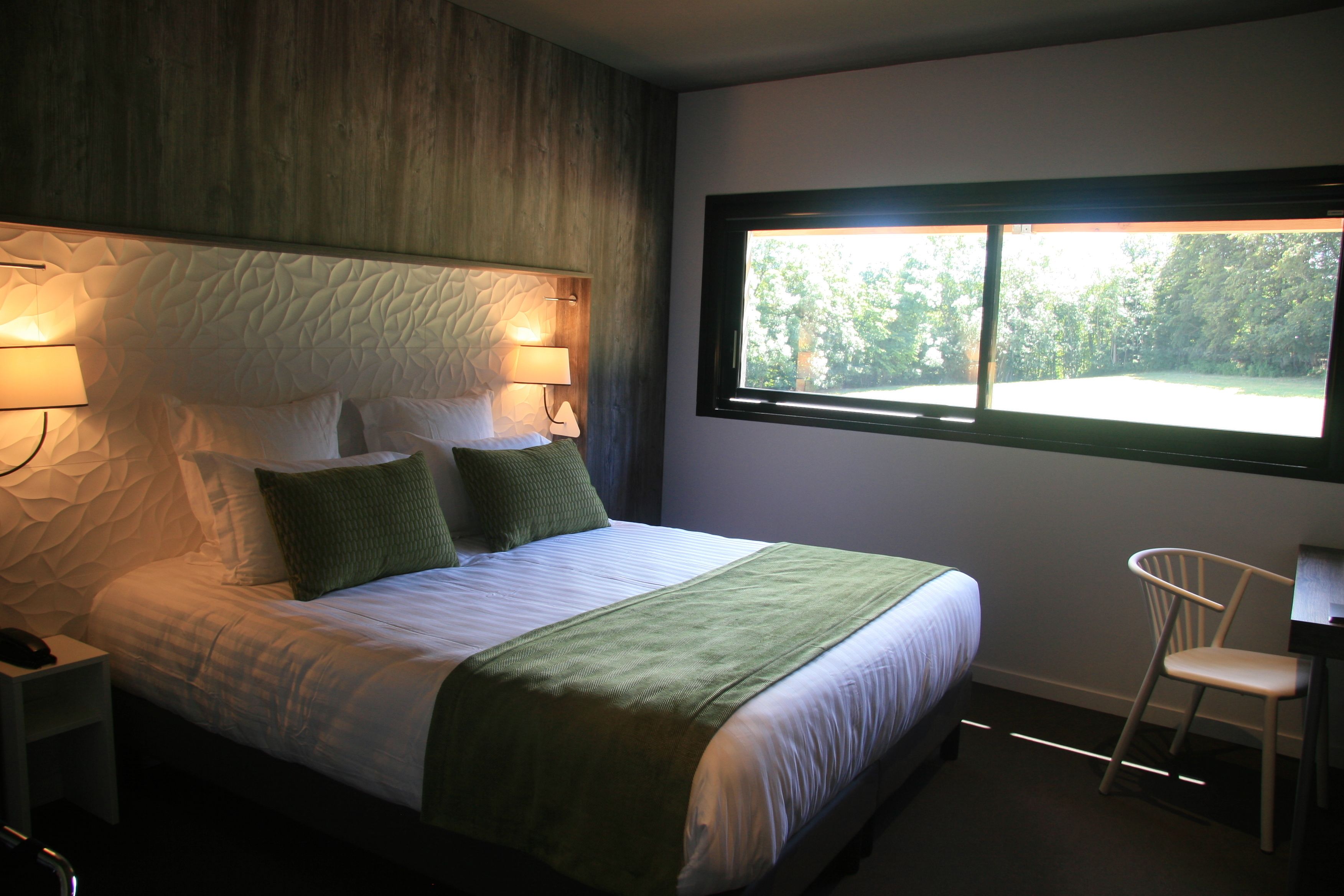 Una cama bien hecha con una manta verde, cabecera de madera y dos lámparas de noche.