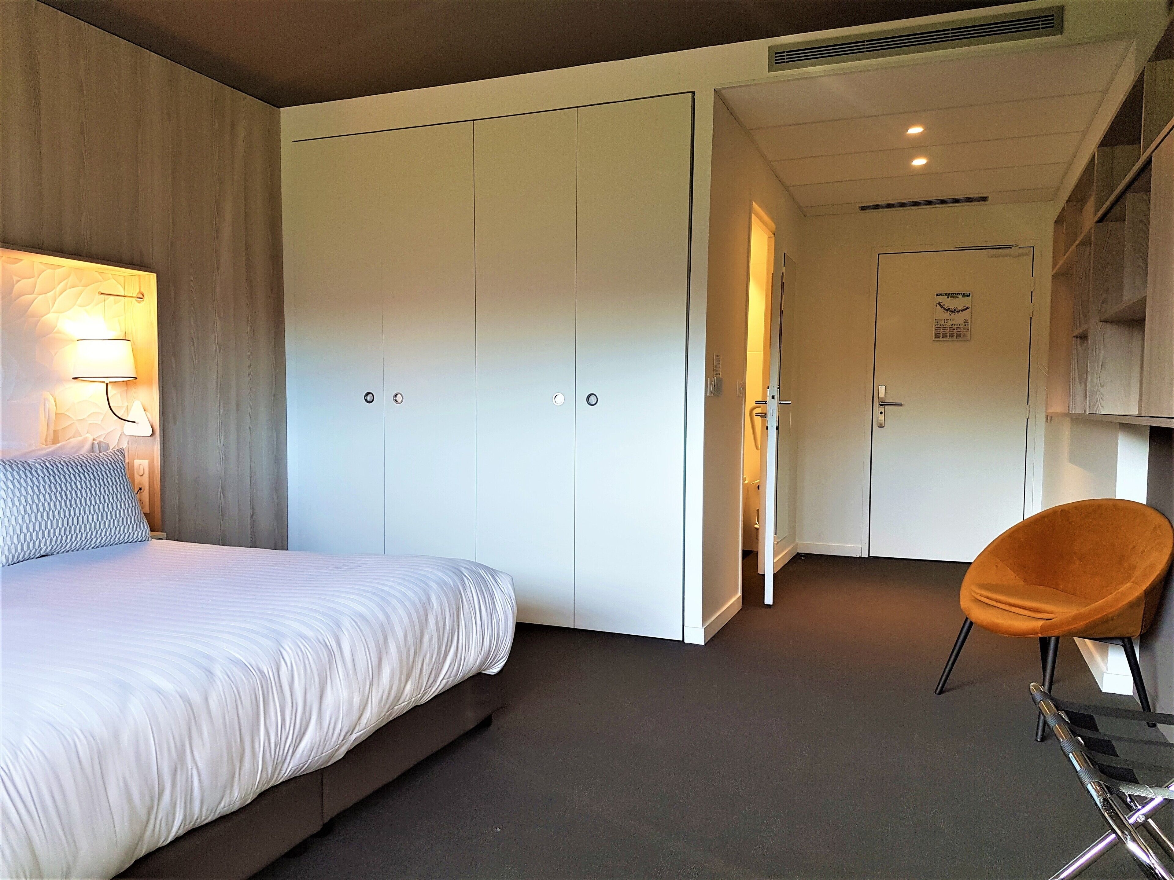 A bedroom with a bed, a wardrobe, a chair, and a nightstand.