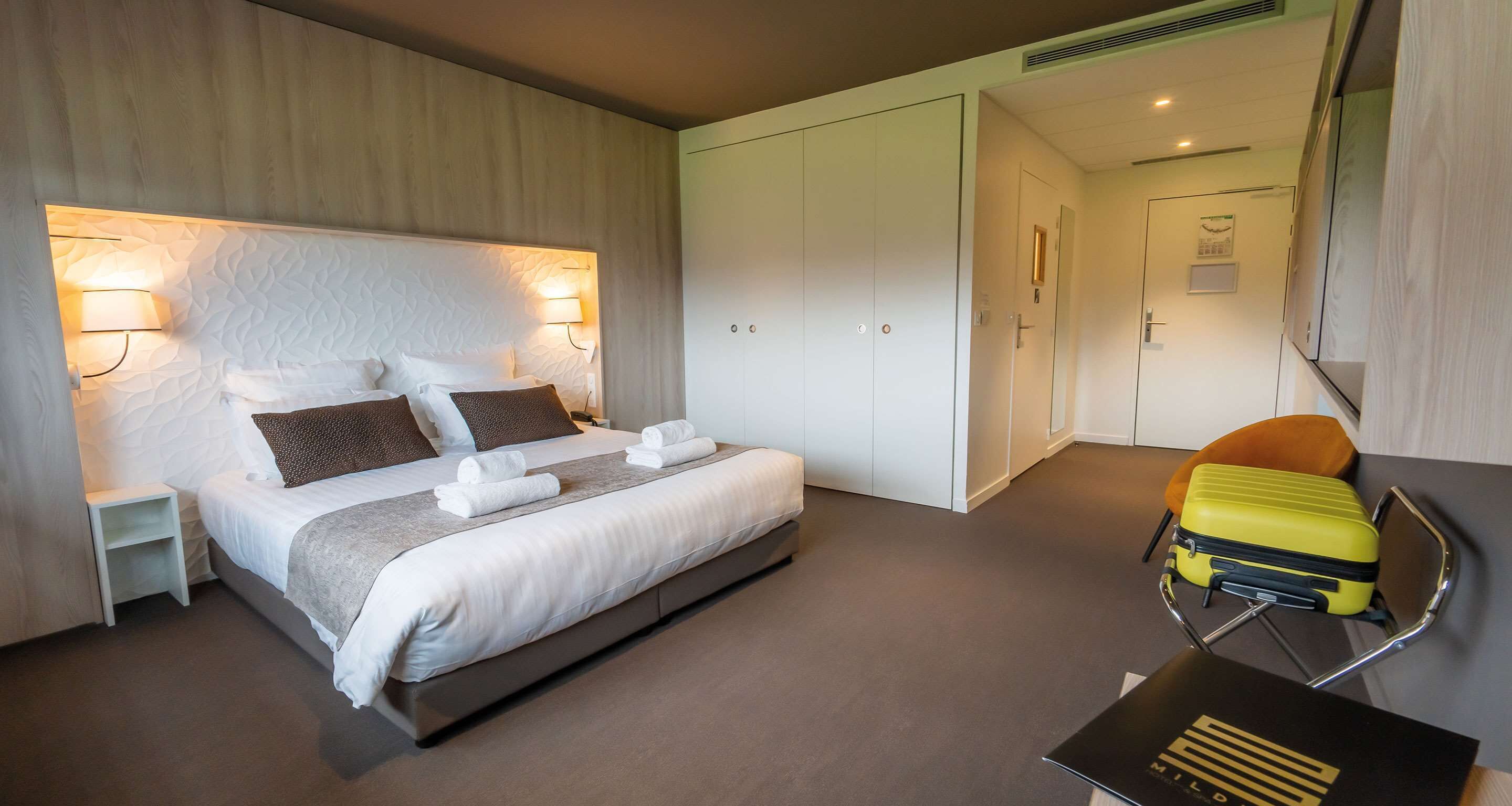 Una habitación de hotel con una cama grande, una mesita de noche, una maleta y un escritorio con un libro.