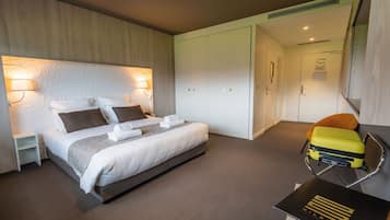 A hotel room with a large bed, a nightstand, a suitcase, and a desk with a book.