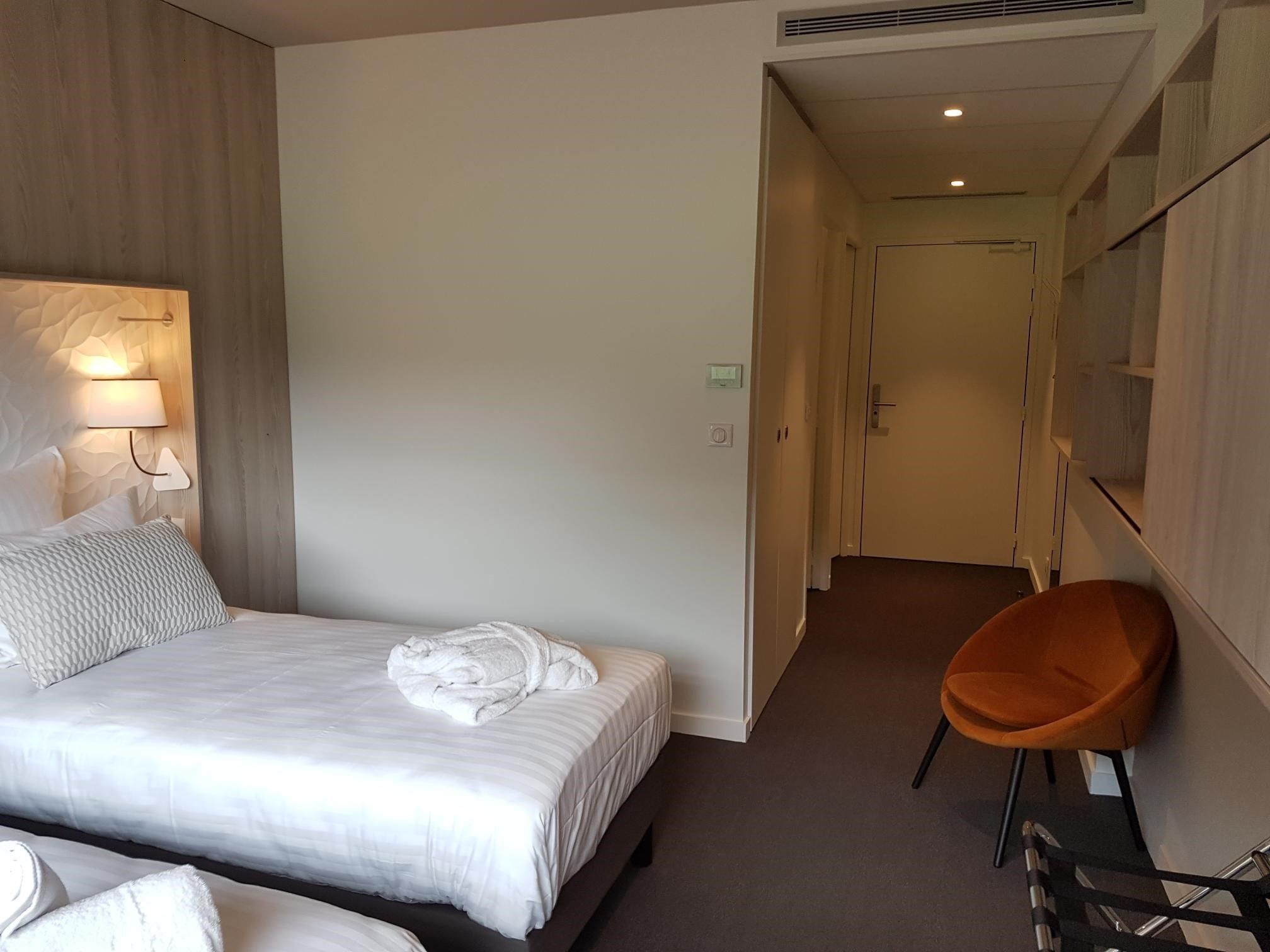 A hotel room with a bed, a chair, a lamp, and a mirror.