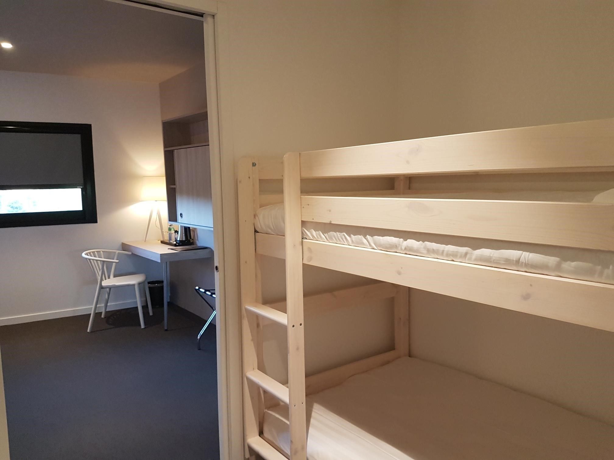 A bunk bed in a room with a desk and chair, a window, and a door.
