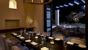 A dining area with a long table set for a meal, a chandelier, and a view of a garden at night. - Grand Solmar at Rancho San Lucas (Cabo San Lucas, Baja California Sur)