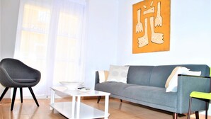 Een woonkamer met een grijze bank, een witte salontafel, een grijze fauteuil en een gele stoel.