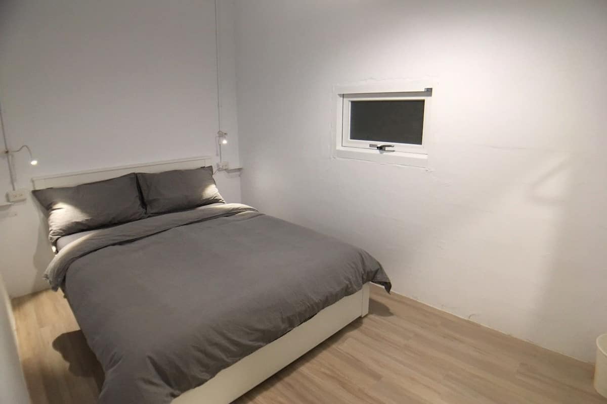 A bedroom with a bed, a small window, and a wall-mounted light fixture.