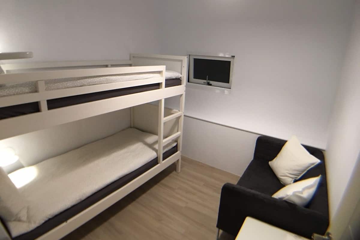 A bunk bed room with a small TV on the wall and a black couch with pillows.